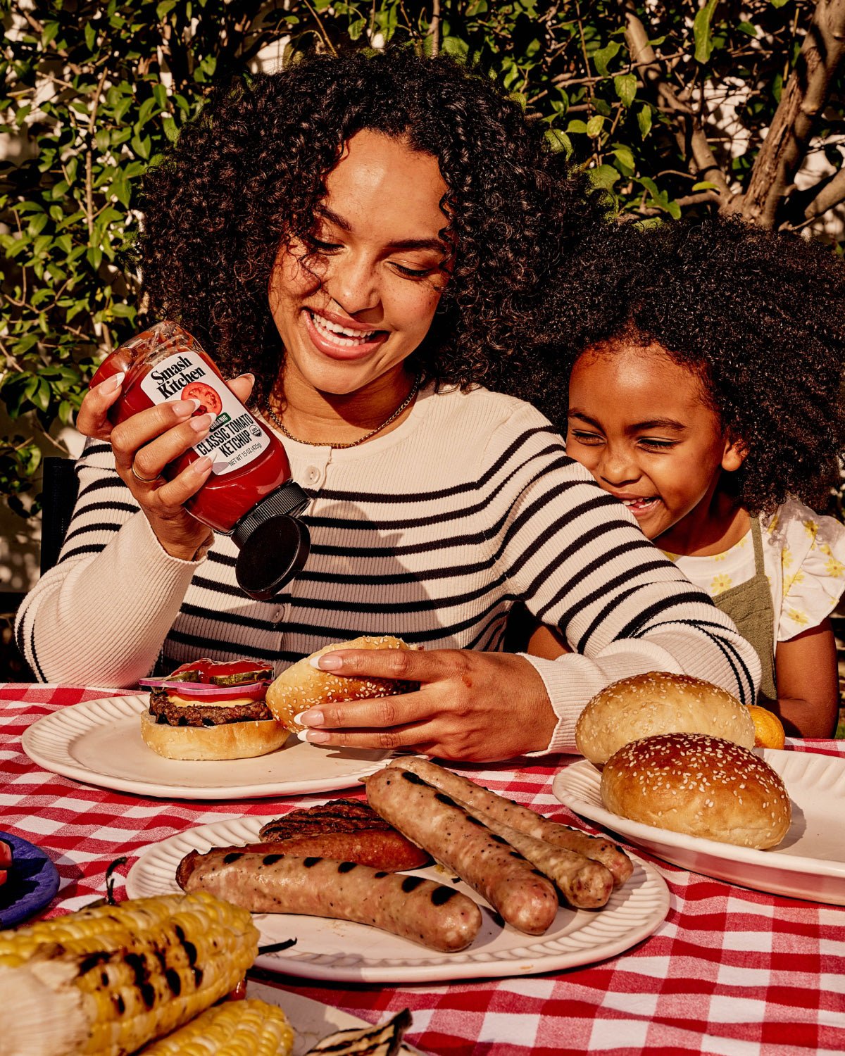 A woman and child at a picnic table eating food and using Smash Kitchen Ketchup.